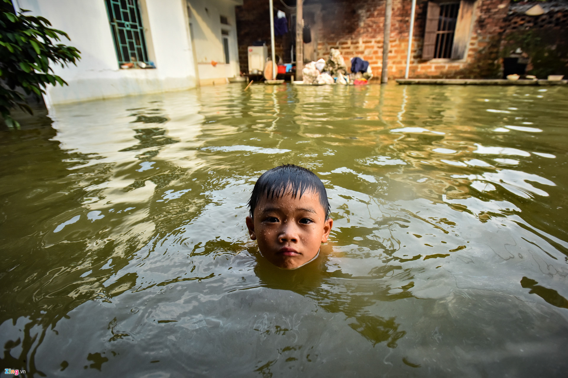 Một cậu bé bơi giữa dòng nước ngập lụt ngay trong nhà mình.