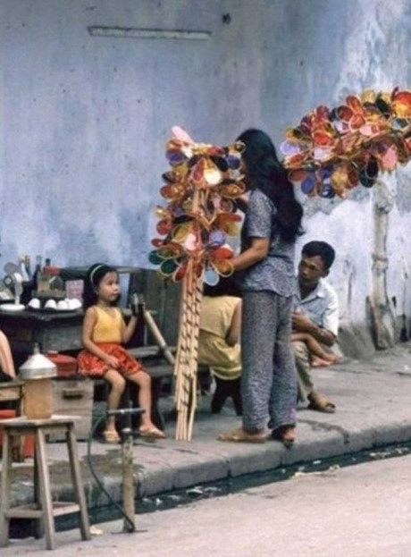 Hà Nội những năm 1990, một cô bán đèn cù quay đang “chào hàng” với một bé gái bên quán nước.