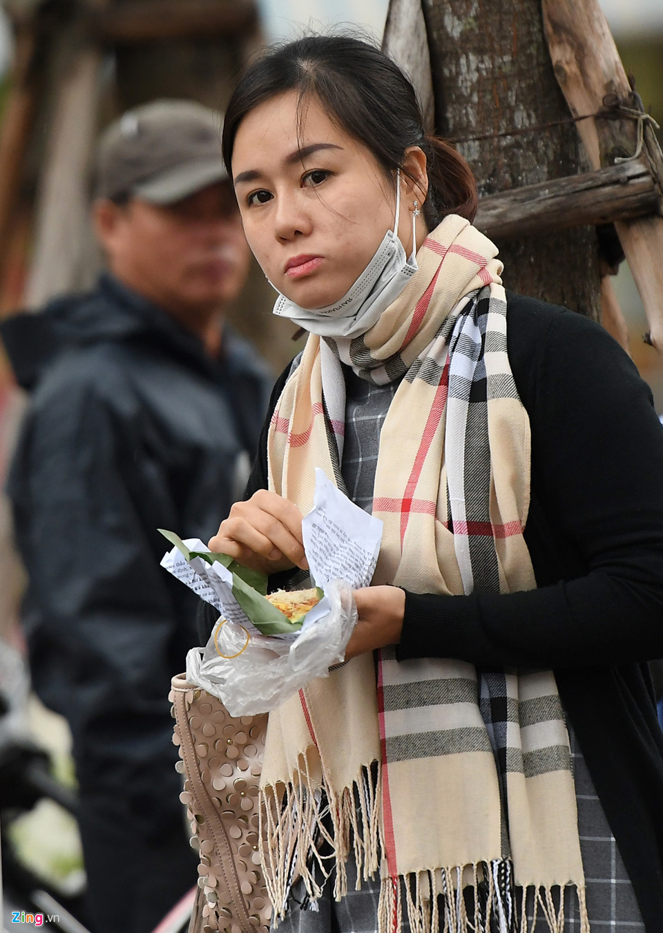 Cô gái  với áo khoác và chiếc khăn quàng cổ ấm áp chờ xe trên vỉa hè Kim Mã, quận Ba Đình cùng bữa sáng nhanh với xôi xéo.